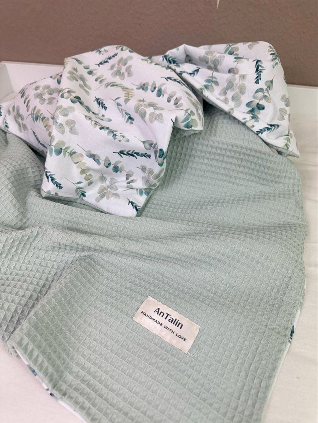 Weiche Babydecke von AnTalin mit Eukalyptuszweigen, zeigt die gemütliche Textur und das natürliche Design.