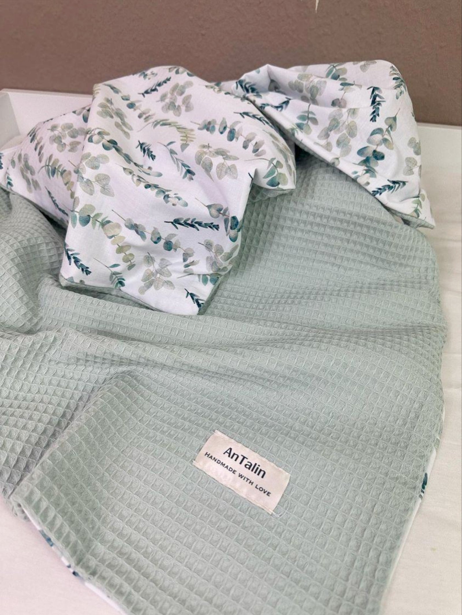 Weiche Babydecke von AnTalin mit Eukalyptuszweigen, zeigt die gemütliche Textur und das natürliche Design.